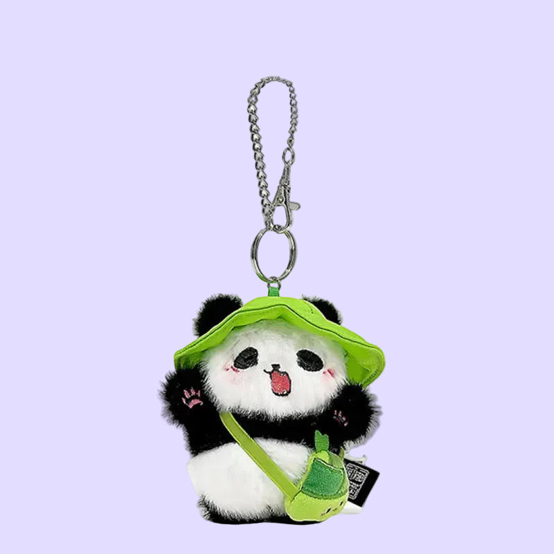 A plush panda keychain charm with a bright green hat, green shoulder bag, and silver metal keychain ring