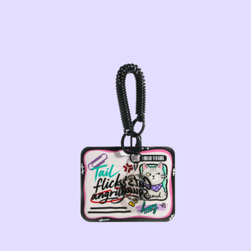 A rectangular keychain or bag charm with a black spiral strap, featuring a pink and white graphic and a cartoon cat illustration, shown on a light gray background with text at the top and bottom.