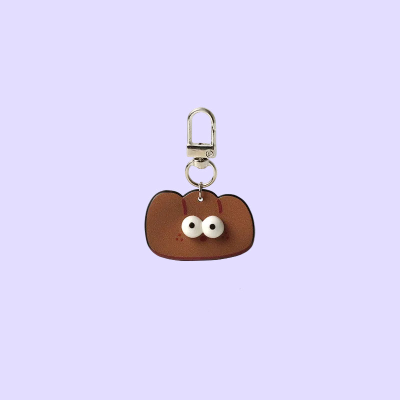 A small brown keychain or bag charm with a silver clasp, featuring a rounded shape, two white bead eyes, and thin red antennae