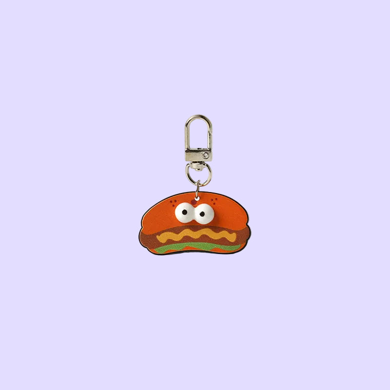 A small novelty keychain charm shaped like a smiling orange-red burger with white eyes, yellow wavy lines, and a green bottom layer, attached to a silver metal clasp.