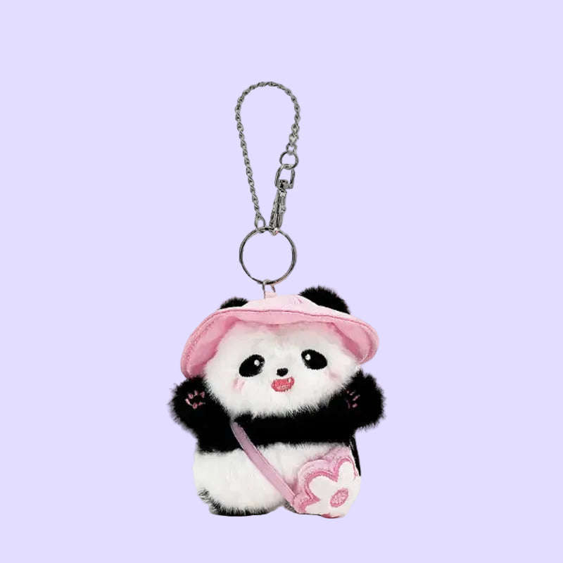 A cute plush panda keychain accessory with a pink hat, pink heart-shaped bag, and silver metal chain